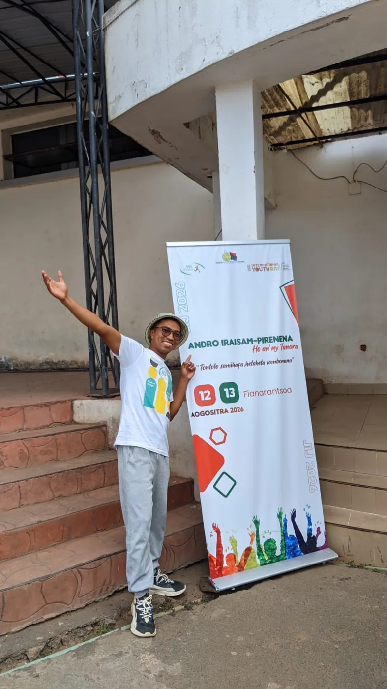 Un bénévole Y4CM pose devant la bannière de la Journée internationale de la jeunesse 2026 à Fianarantsoa.